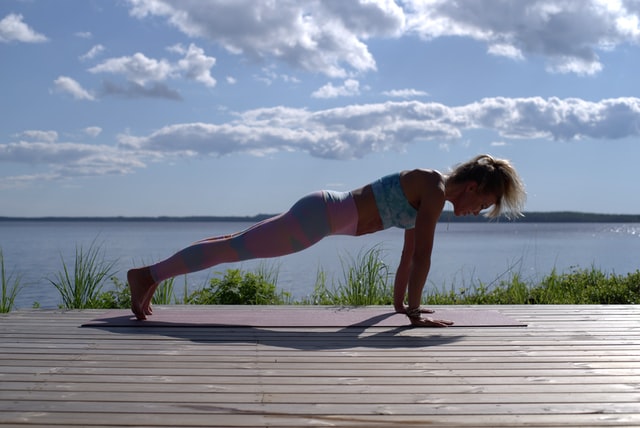 A woman in workout clothes doing a plank on a wooden deck next to a lake