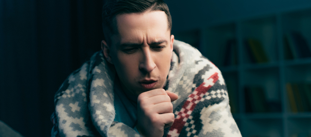 Sick young man with blanket coughing