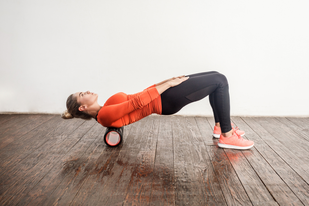 a woman wearing exercise clothing using a foam roller on her back muscles
