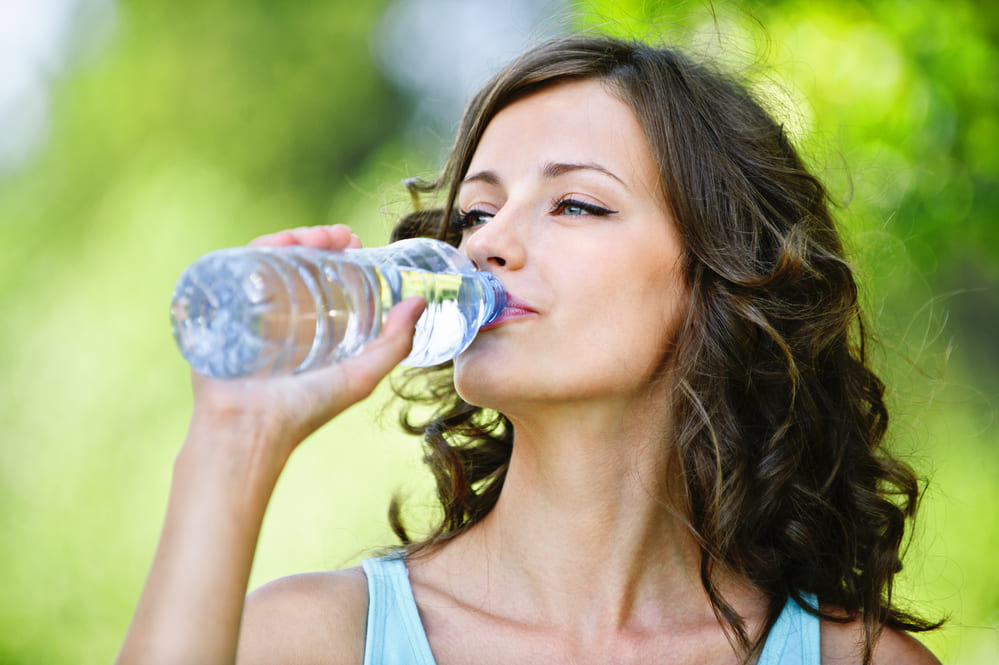 a woman outside drinking from a plastic water bottle