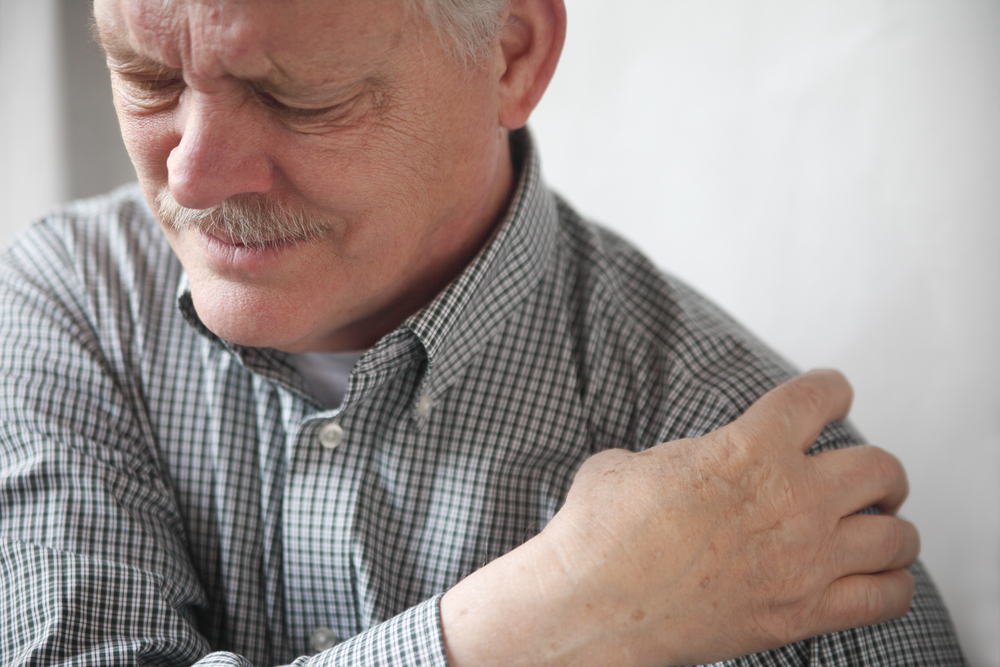 An older man clutches his shoulder in pain. 