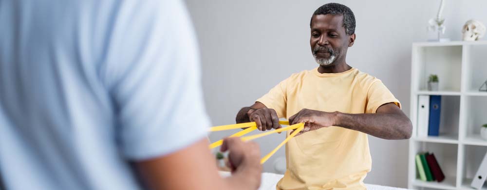 A man uses a resistance band to exercise in a physical therapist's office.