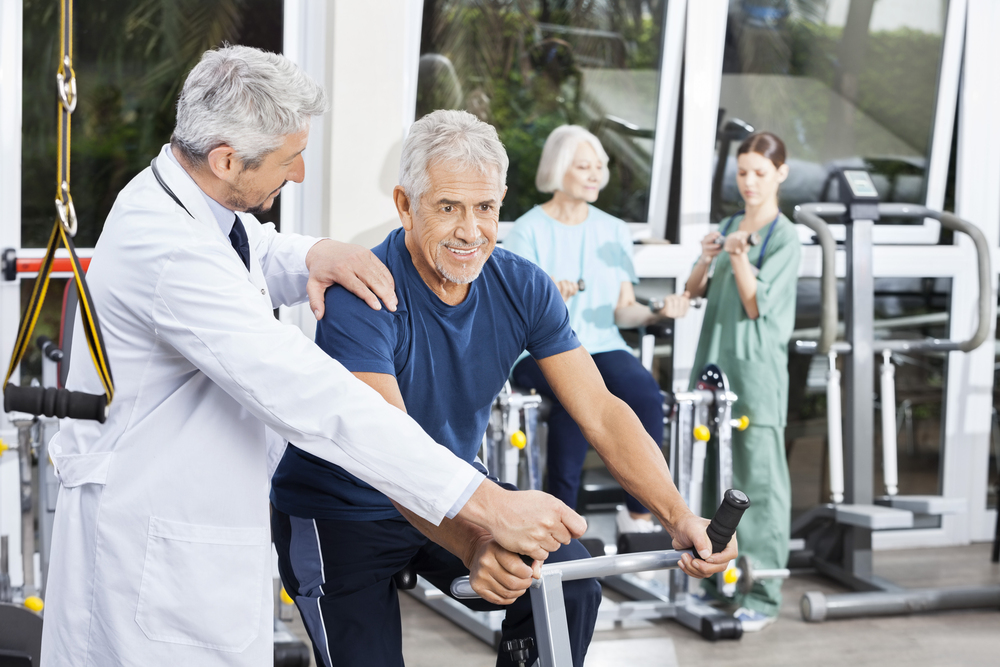 Doctor Instructing Senior Man On Exercise Bike